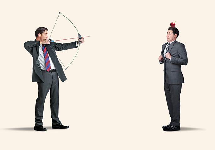Man with bow and arrow shoots at apple on his opponent's head.