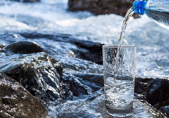 Water glass into which mineral water is poured, stands in rushing river.