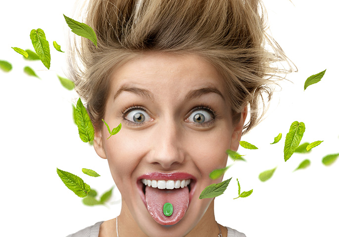Woman with widened eyes and green candy on her tongue from which mint leaves fly away, stands her hair up.