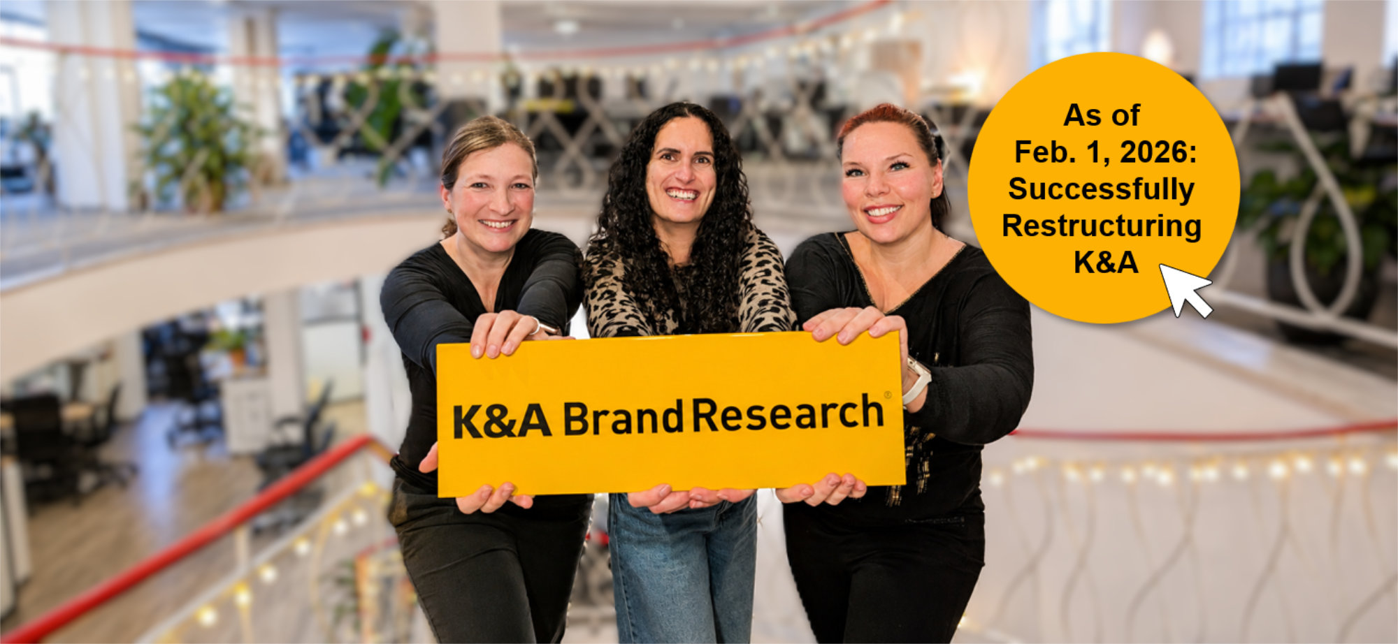 The three founders of K&A BrandResearch GmbH—Anja Postler, Irena Leuthold, and Christina Kisskalt—are holding a yellow sign together that reads "K&A BrandResearch." In the background is an office setting, along with a yellow button featuring a clickable arrow and the text: "Since Feb 1, 2026: Successful restructuring of K&A."
