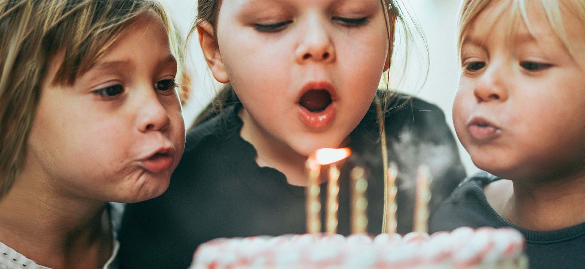 Three young girls blowing out candles on birthday cake.