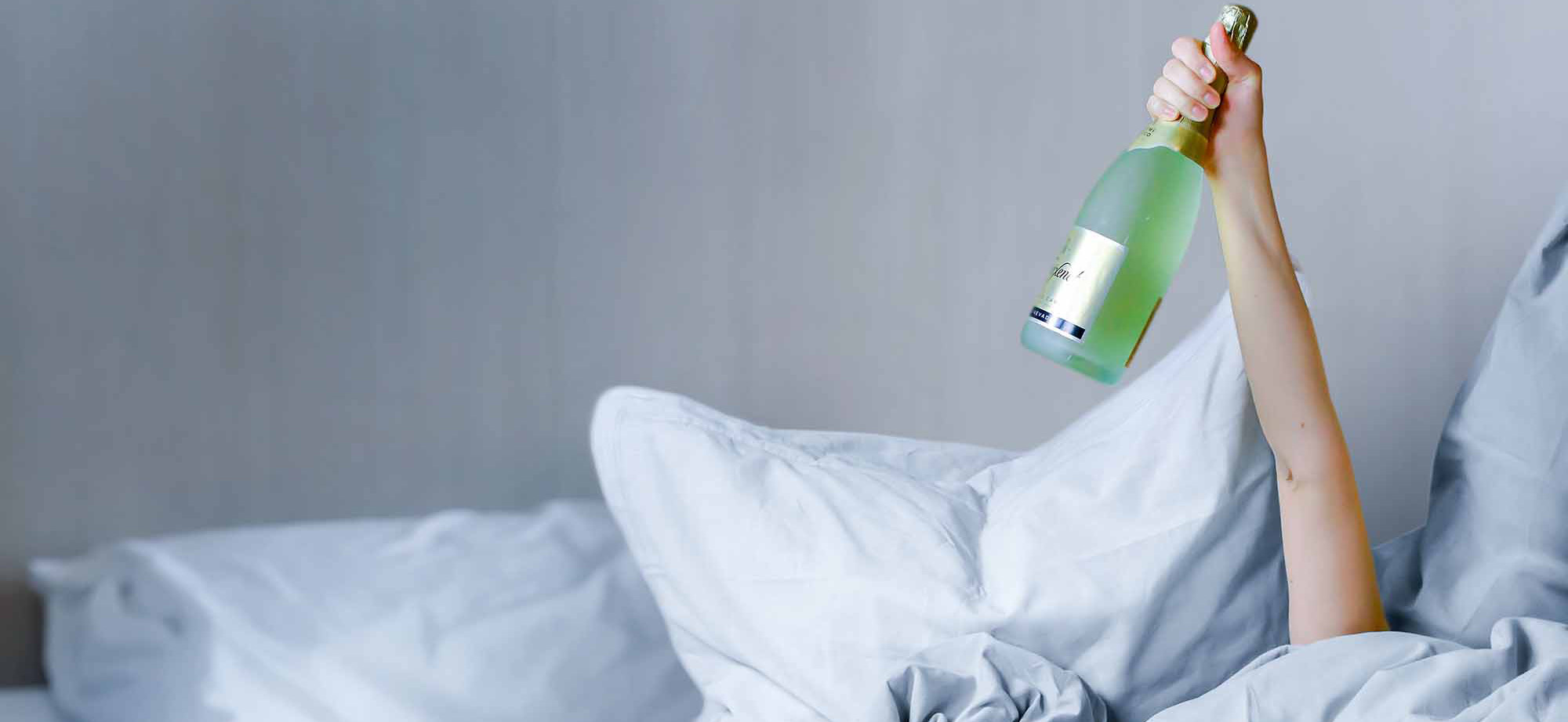 Woman arm holding up sparkling wine bottle in bed.