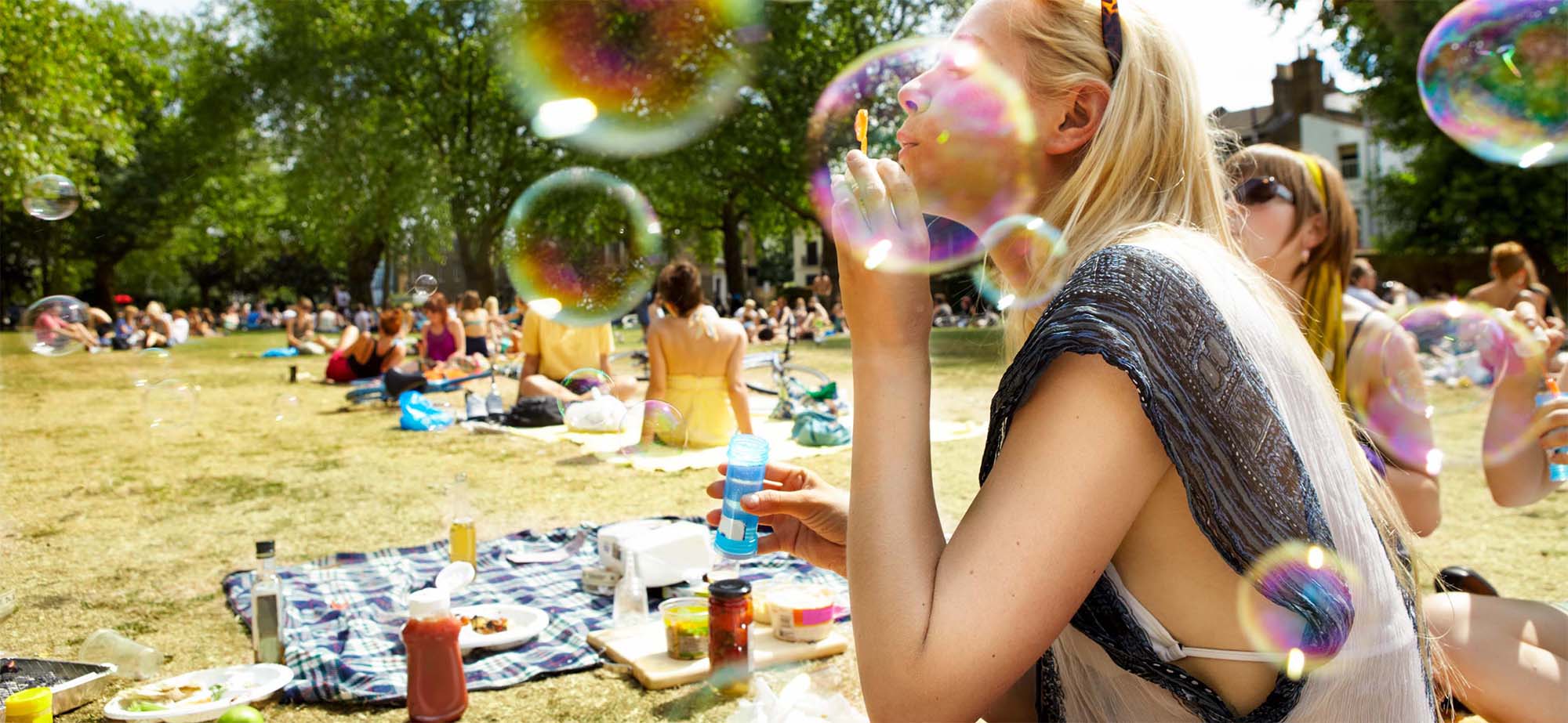 Woman lying on the grass with others at picnic blowing soap bubbles.