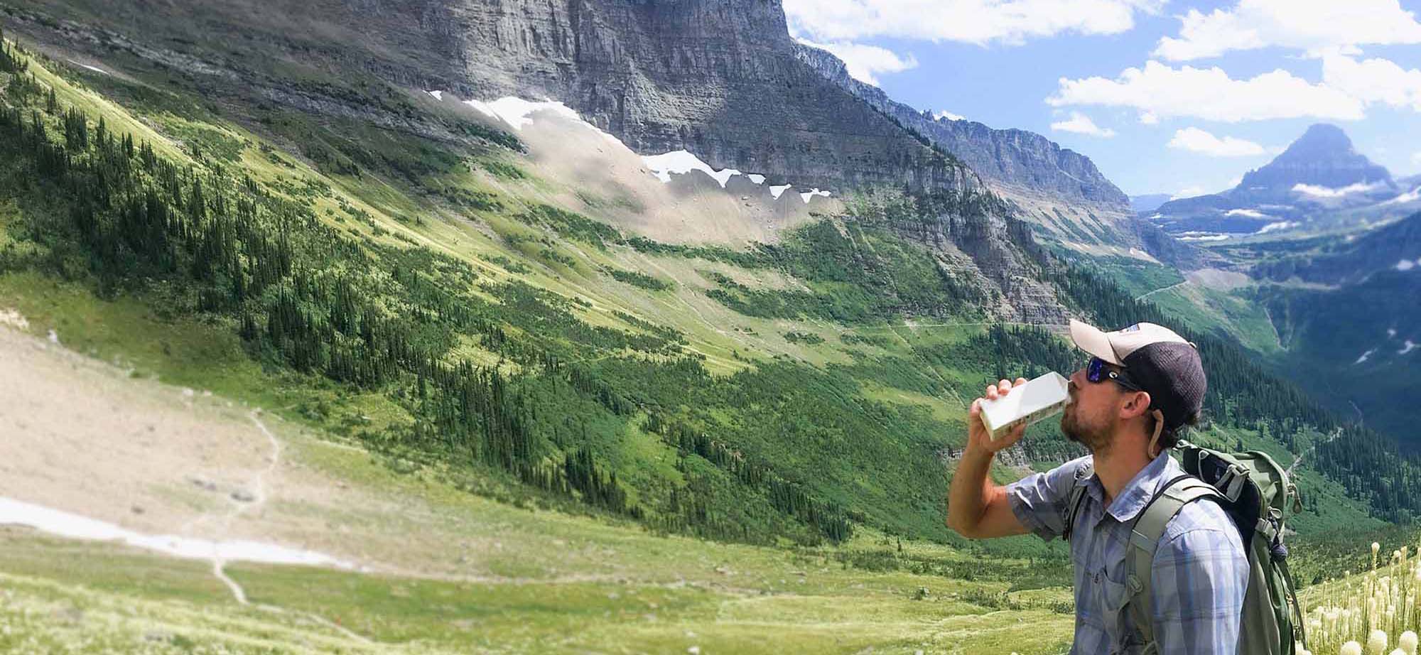 Hiker in the mountains drinks from tetrapack.