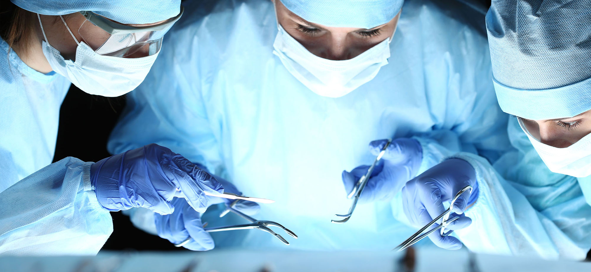 Surgeons in blue scrubs operate with various surgical instruments.