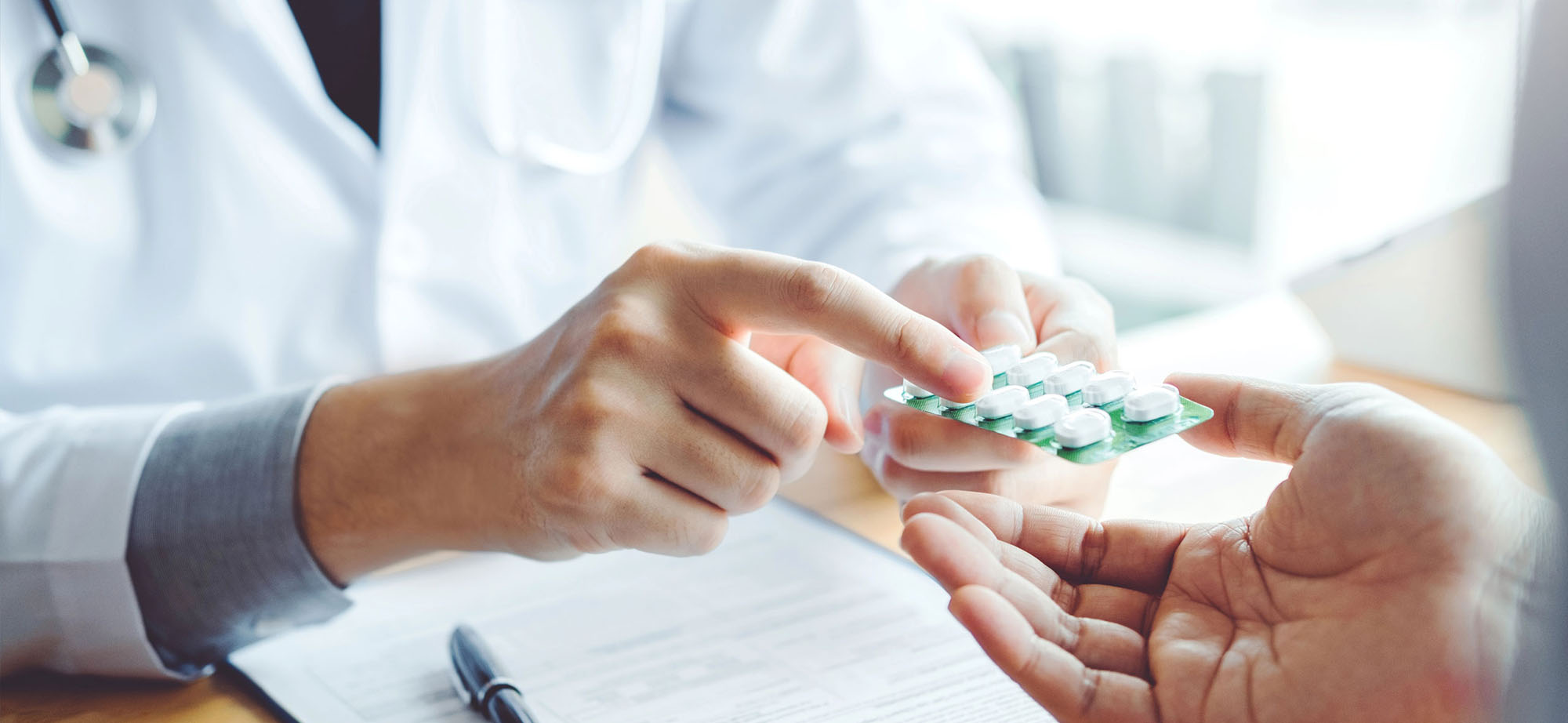 A doctor hands a packet of pills to a patient and points at it.