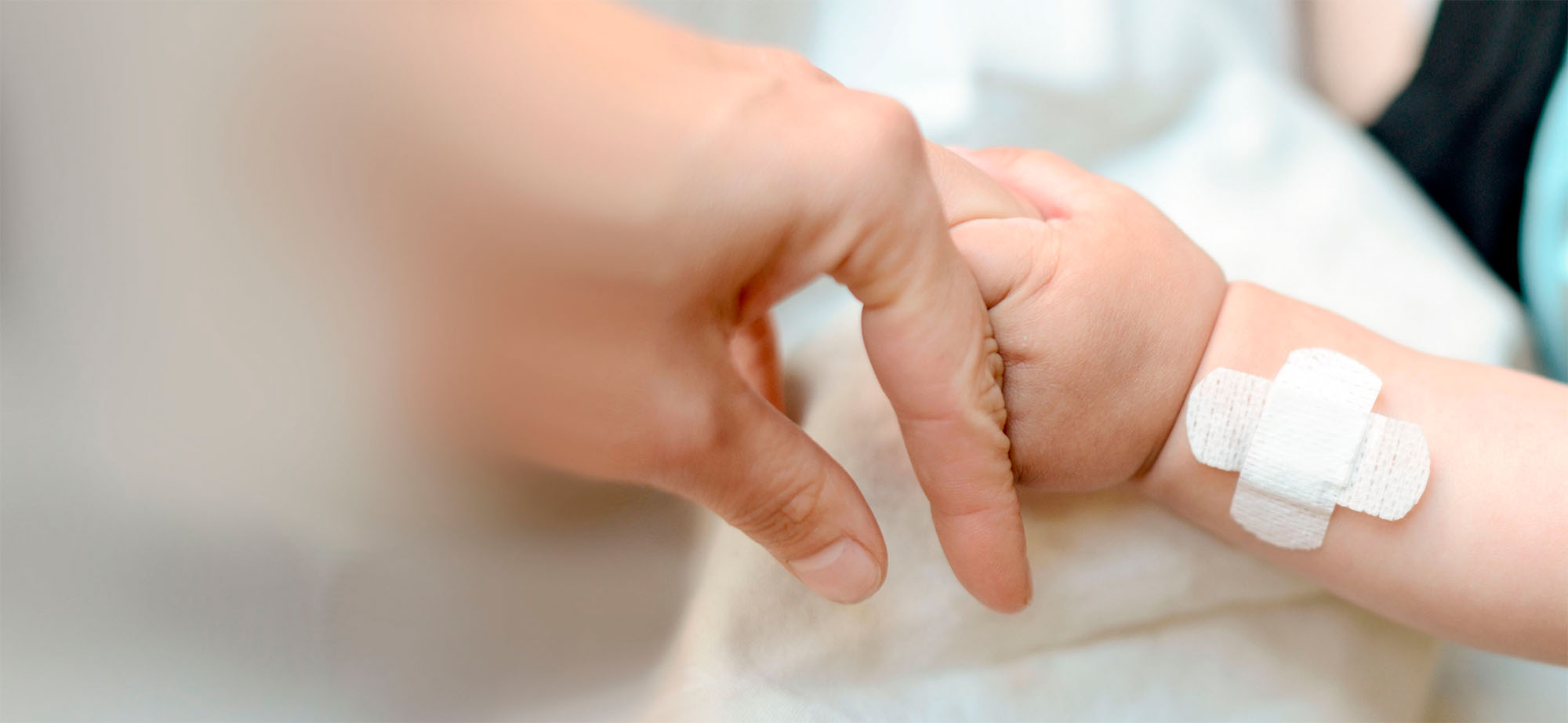 Baby hand with plaster holds adult finger.