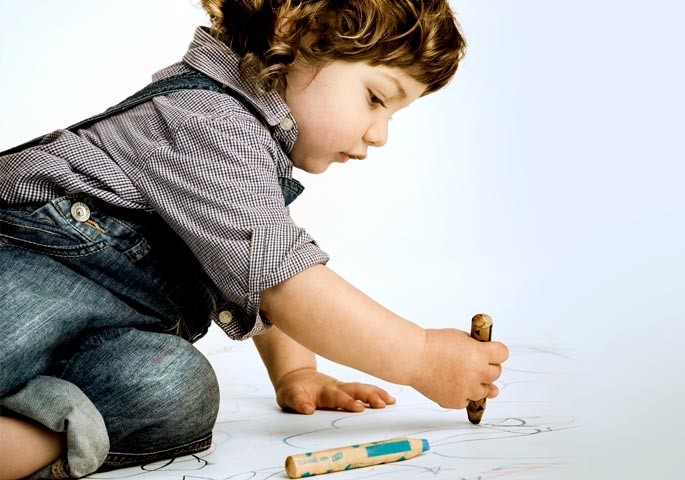 Kleinkind malt mit dicken Stiften auf dem Boden