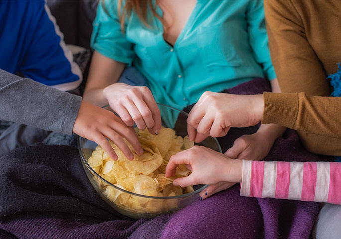 Several hands grab into bowl with chips.