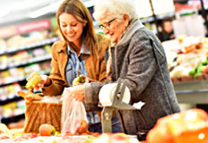 Junge und ältere Frau lachend in der Obst- und Gemüseabteilung eines Handelsgeschäfts.