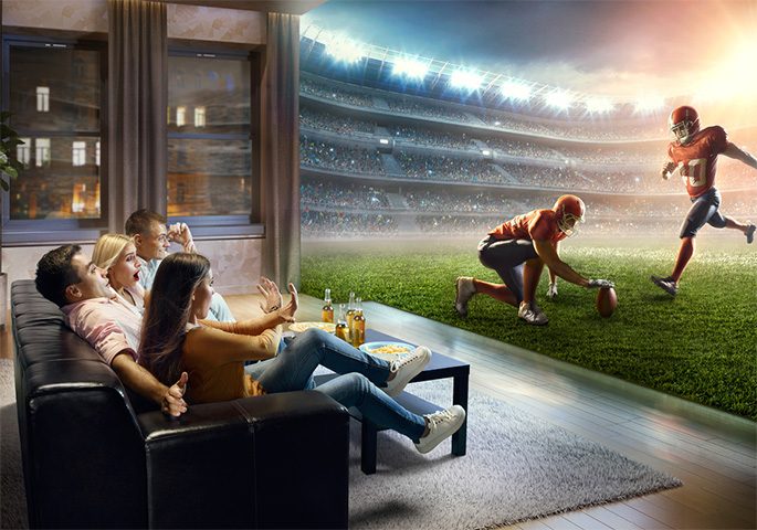 Friends watch football on the couch. Instead of watching TV, it looks like they're right in the stadium.